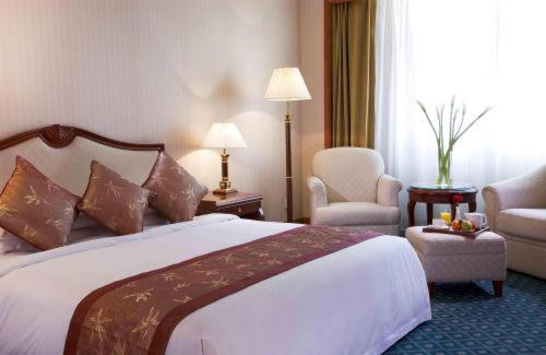a hotel room with a large bed and two chairs at Swissôtel Hefei Grand Park in Hefei