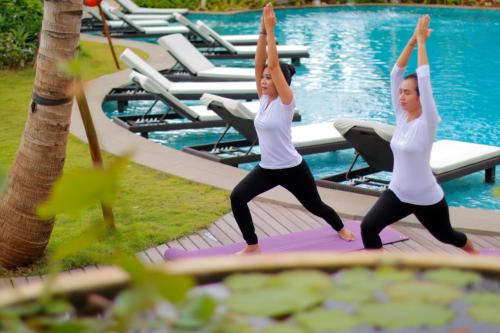 two women doing yoga by a swimming pool at Royal Tulip Springhill Resort Jimbaran in Jimbaran