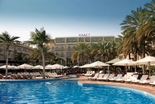 ein Pool mit Stühlen und Sonnenschirmen sowie ein Hotel in der Unterkunft Grand Hyatt Muscat in Muscat