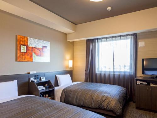 a hotel room with two beds and a television at Hotel Route Inn Minami Yokkaichi in Yokkaichi