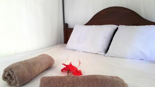a bed with white sheets and a red flower on it at Era Holiday House in Mirissa