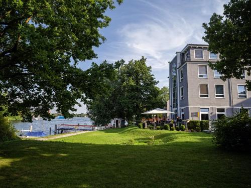 a building on a lawn next to a body of water at Hotel am Schloß Köpenick by Golden Tulip in Berlin