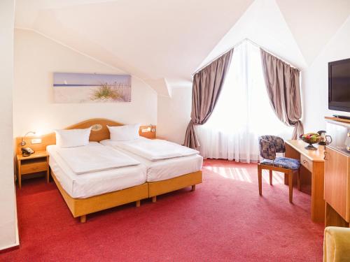 een slaapkamer met een bed, een bureau en een televisie bij Hotel Dänischer Hof Altenholz by Tulip Inn in Altenholz