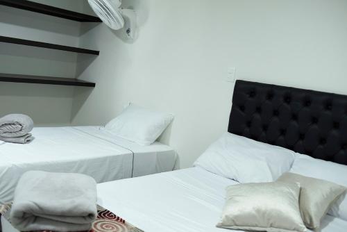 twee bedden met witte lakens en een zwart hoofdeinde in een kamer bij Hotel Palma Rosa Medellin in Medellín