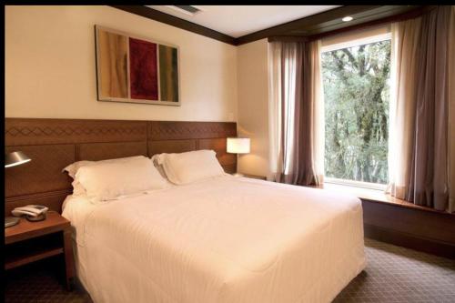 Un dormitorio con una gran cama blanca y una ventana en Apartamento Mountain Village, en Canela