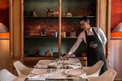 a man in an apron standing over a table with glasses at Hotel L'Iglesia in El Jadida