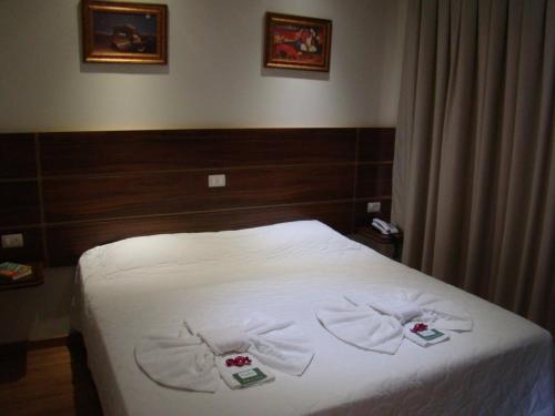 a bedroom with a bed with white sheets and two towels at Pissoloto Hotel in Sertanópolis