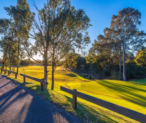 a wooden fence next to a green field with trees at Oaks Cypress Lakes Resort in Pokolbin