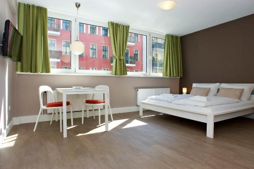 a bedroom with a bed, chair, table and window at Apartmenthouse Berlin - Am Görlitzer Park in Berlin
