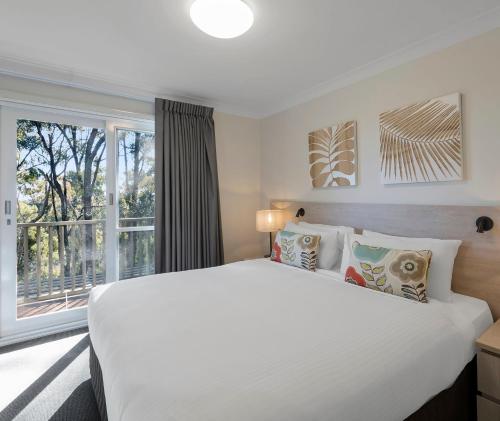 a bedroom with a large white bed and a window at Oaks Cypress Lakes Resort in Pokolbin