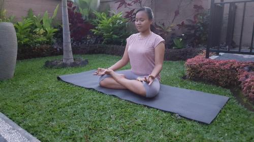 a woman sitting in a yoga pose on the grass at Umayuri Inn in Ubud