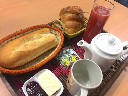 Auf einem Tisch stand ein Tablett mit Brot und Gebäck sowie eine Teekanne. in der Unterkunft TANA-JACARANDA in Antananarivo