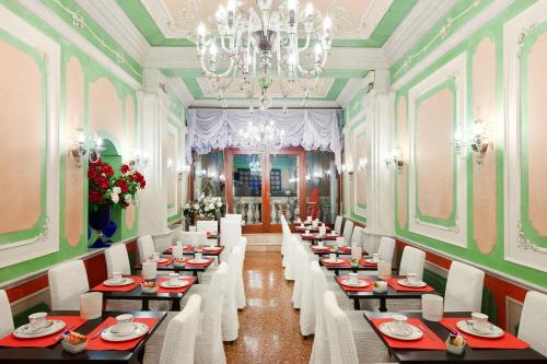 un comedor con mesas, sillas blancas y una lámpara de araña en Residenza d'Epoca San Cassiano, en Venecia