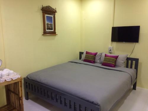 a bedroom with a bed with pink pillows and a tv at Smilingface guesthouse in Sukhothai