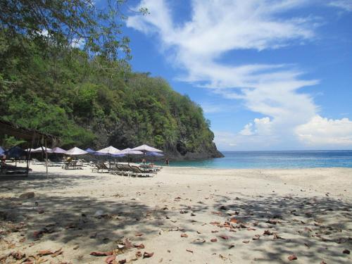 a beach with umbrellas and chairs and the ocean at Bukit Asri Lodge in Seraya