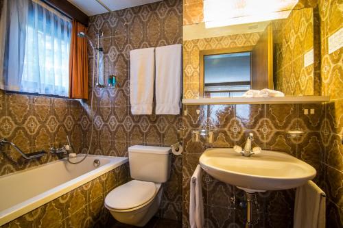 a bathroom with a toilet and a sink and a tub at Hotel La Collina in Saas-Fee