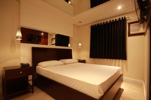 um quarto com uma grande cama branca e uma mesa de cabeceira em Motel Atos ADULTS ONLY em São Paulo
