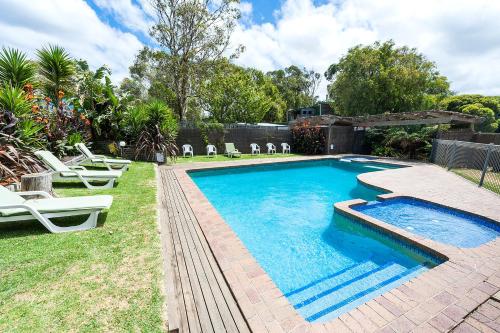 a swimming pool with lounge chairs next to a yard at Motel Marengo in Apollo Bay