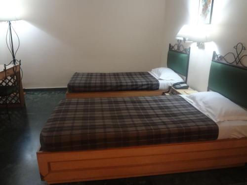 two beds sitting in a room with two lamps at The Hotel Airport in Vadodara
