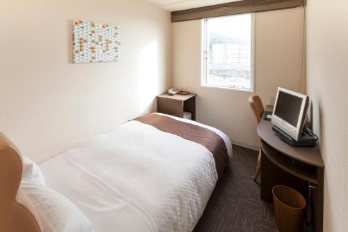a hotel room with a bed and a desk with a television at Sunsky Hotel in Kitakyushu