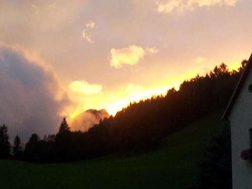 a sunset over a mountain with trees and a house at Ferienwohnung am Bauernhof Zechner Heidi in Flattach