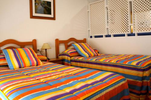 1 dormitorio con 2 camas con sábanas de rayas coloridas en Hotel Apartamentos Kantara Al-Saif, en Alcántara