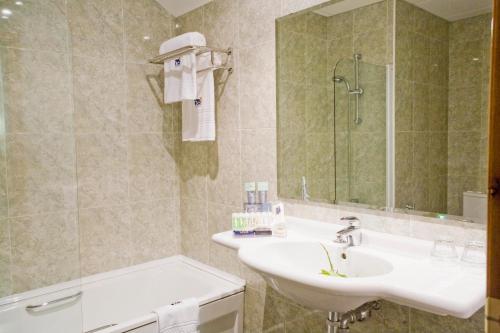 a bathroom with a sink and a mirror and a tub at Hotel Oca Vermar in Aios