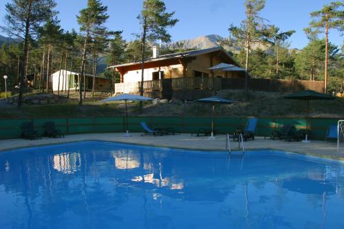 une grande piscine bleue avec une maison en arrière-plan dans l'établissement Parc Résidentiel de Loisir : Le Loup Blanc du Riou, à Barcelonnette