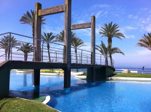 un puente sobre una piscina con palmeras y el océano en Apartamento playa Samil en Vigo