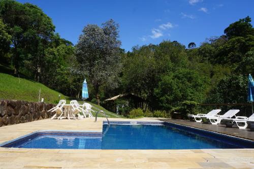 a swimming pool with two white chairs and a statue at Pousada da Mata in Cunha