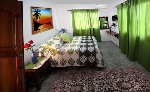 1 dormitorio con cama, mesa y cortinas verdes en Residencial Estephany, en Sosúa