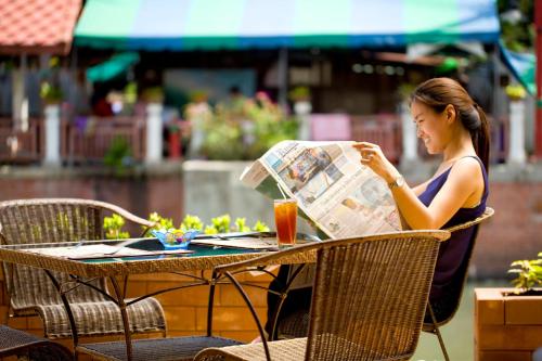 a woman sitting at a table reading a newspaper at Korbua House in Bangkok