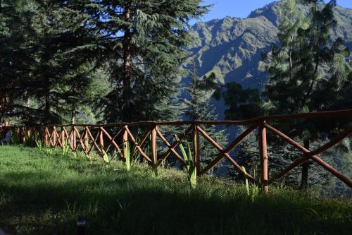 a wooden fence in a field with mountains in the background at Kudrat - A Boutique Homestay- Tirthan Valley in Banjār