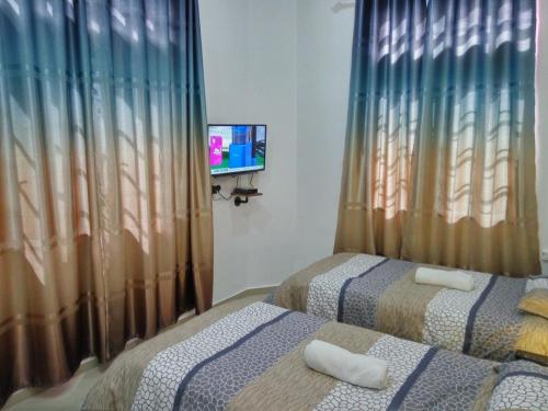 two beds in a room with a tv and curtains at H2O Apartment in Cameron Highlands