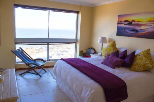 a bedroom with a bed and a chair and a large window at Breathtaking views in Blouberg! in Bloubergstrand