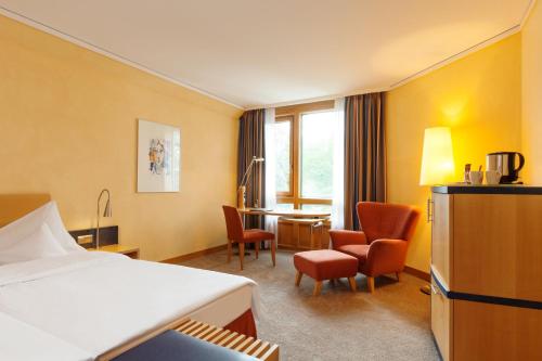 a hotel room with a bed and chairs and a desk at Vienna House by Wyndham Remarque Osnabrück in Osnabrück