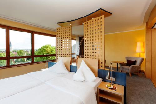 a hotel room with a large white bed and windows at Vienna House by Wyndham Remarque Osnabrück in Osnabrück