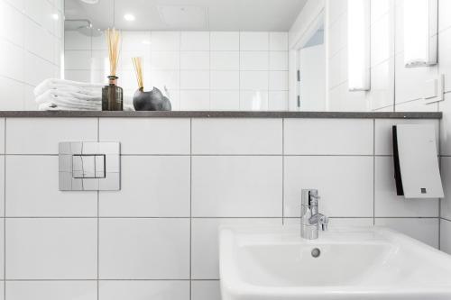 a white tiled bathroom with a sink and a mirror at Biz Apartment Hammarby Sjöstad in Stockholm