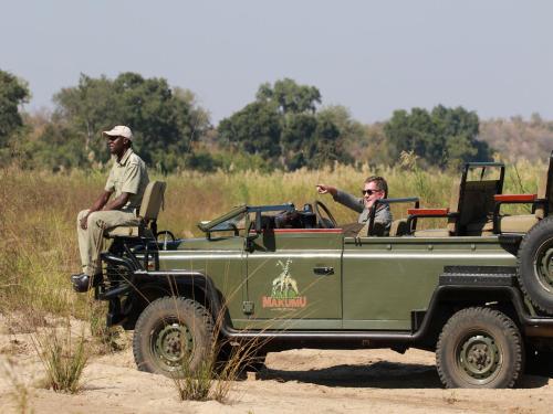 two men riding in a green jeep on a field at Makumu Private Game Lodge in Klaserie Private Nature Reserve
