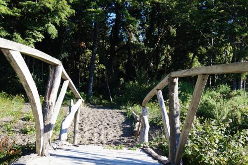 a wooden bridge over a sandy path with trees at Cabañas Domos May-Ling in Ensenada