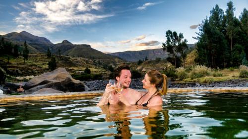 a man and a woman in the water with a glass of wine at Colca Lodge Spa & Hot Springs in Yanque