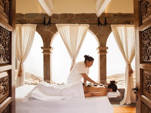 a woman laying on a bed while a woman is getting ready at Inkaterra La Casona Relais & Chateaux in Cusco