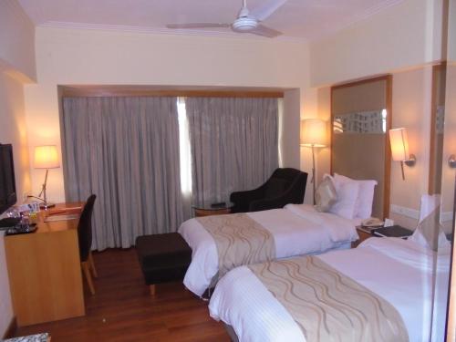 a hotel room with two beds and a chair at Lords Plaza Ankleshwar in Ankleshwar