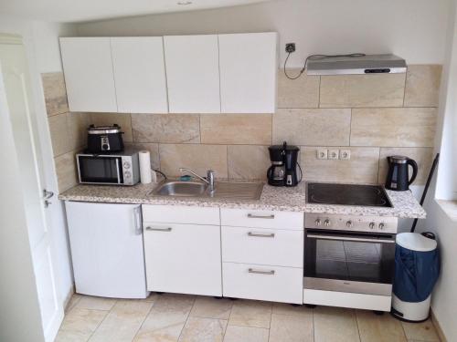 eine kleine Küche mit weißen Schränken und einer Spüle in der Unterkunft Haus auf der alten Düne in Prerow