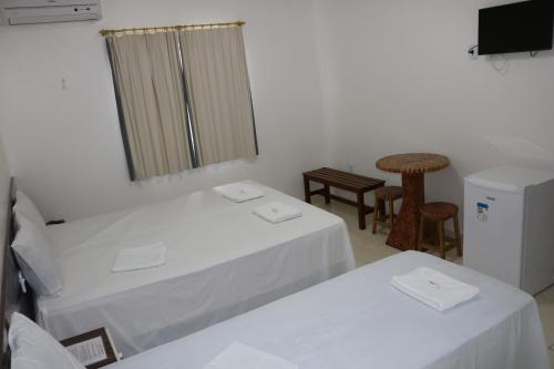 a room with two white beds and a television at Pousada Sol Nascente in Piranhas