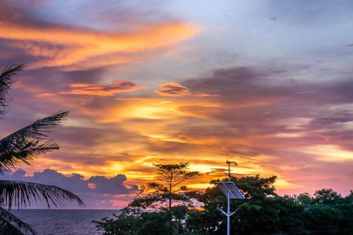 a sunset over the ocean with trees and a street light at Visal Sak Guesthouse in Kep