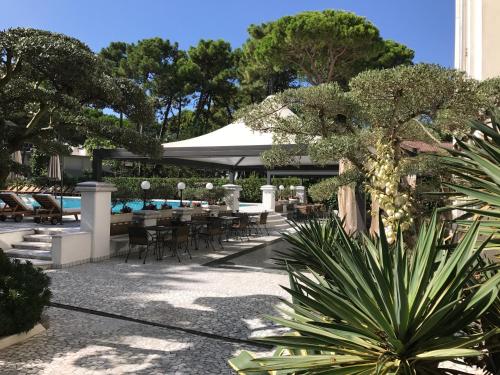 an outdoor patio with tables and chairs and trees at Hotel Greif in Lignano Sabbiadoro