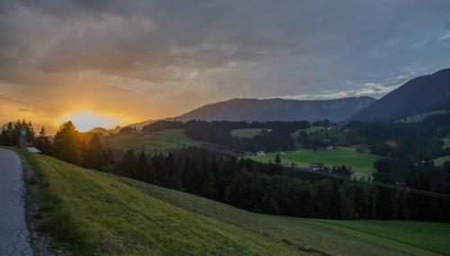 a sunset over a green hill with a road at Alpenhaus Dachstein.Zauber in Abtenau