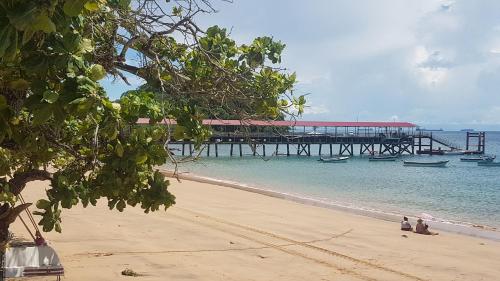 a beach with a pier and two people sitting on the sand at Cerrito Tropical Eco Lodge in Taboga