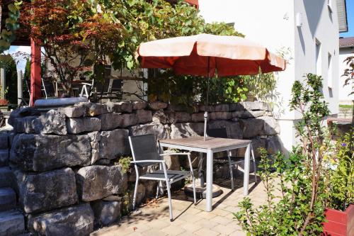 a table and chair under an umbrella next to a stone wall at BodenSEE Apartment Meckenbeuren Neuhaldenstrasse in Meckenbeuren